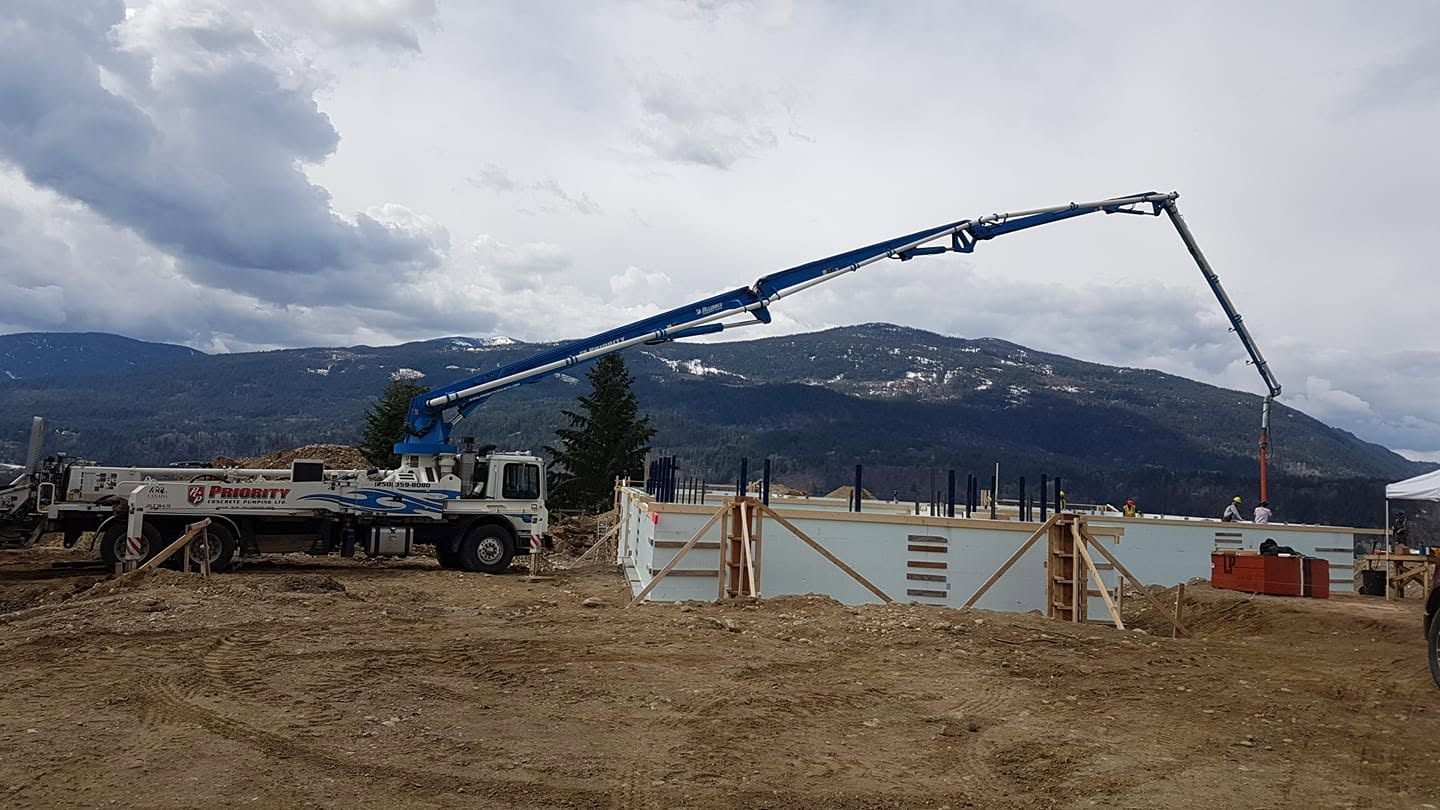 A PNT skid-steer and dump trailer parked next to fresh framing on a mountain build site